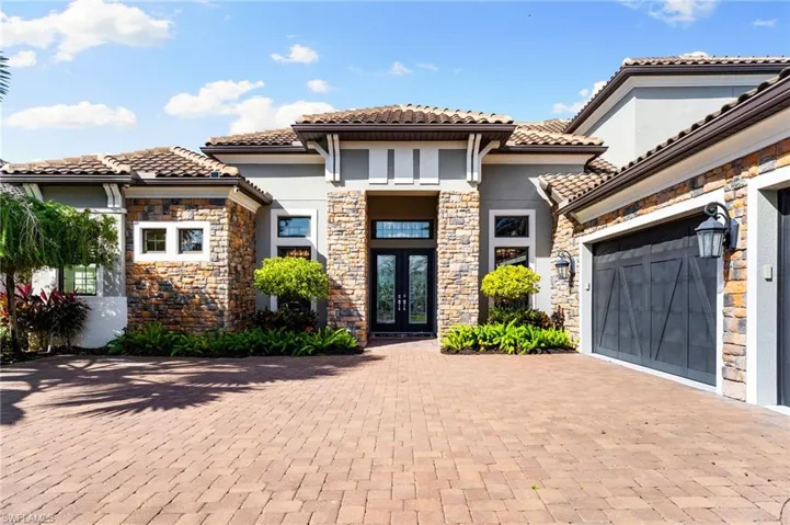 View of front facade featuring french doors, stucco siding, decorative driveway, stone siding, and a tile roof