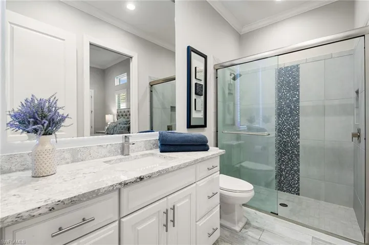 Ensuite bathroom with ornamental molding, vanity, and a shower stall