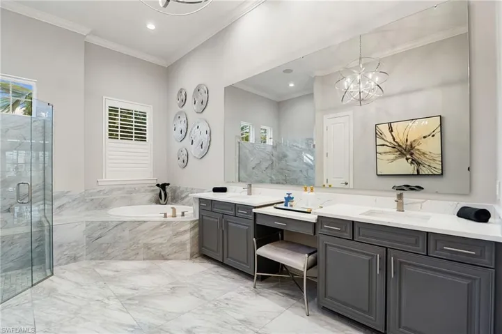 Full bathroom with a chandelier, light marble finish floors, a garden tub, double vanity, and crown molding