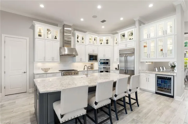 Kitchen with white cabinetry, light stone countertops, wine cooler, recessed lighting, and a kitchen island with sink