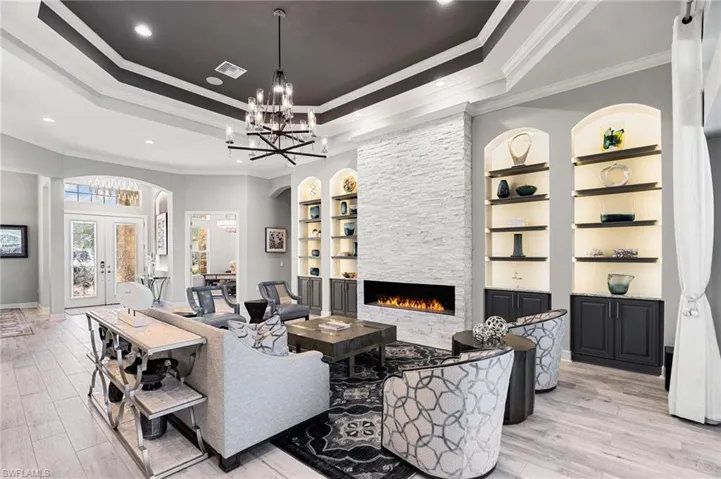 Living room featuring built in shelves, ornamental molding, a stone fireplace, light wood finished floors, and arched walkways