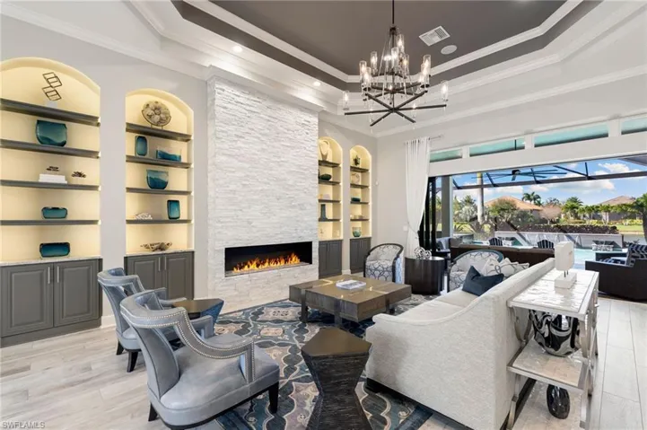Living area featuring built in shelves, a stone fireplace, ornamental molding, a sunroom, and light wood finished floors