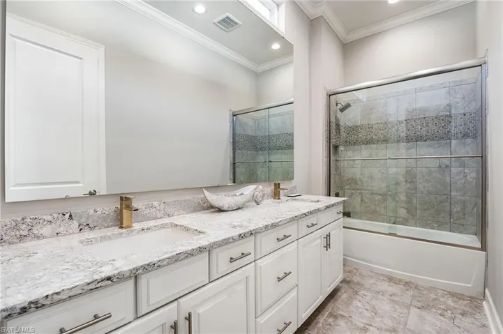 Bathroom with enclosed tub / shower combo, double vanity, ornamental molding, and recessed lighting