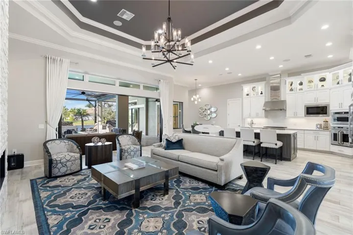Living area featuring ornamental molding, light wood finished floors, recessed lighting, a tray ceiling, and a chandelier