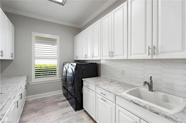 Laundry area with cabinet space, ornamental molding, light wood finished floors, and separate washer and dryer