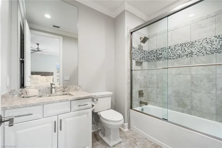Bathroom featuring crown molding, enclosed tub / shower combo, vanity, ceiling fan, and light tile patterned floors