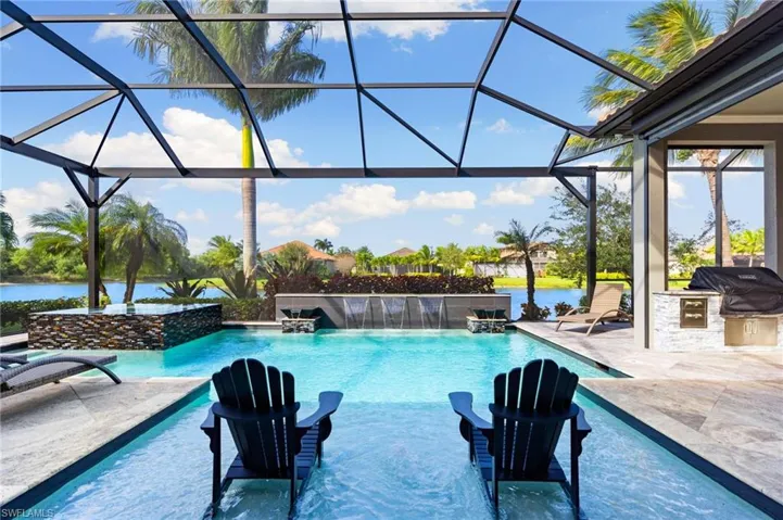 Outdoor pool featuring a sunroom, glass enclosure, a patio area, an outdoor kitchen, and a water view