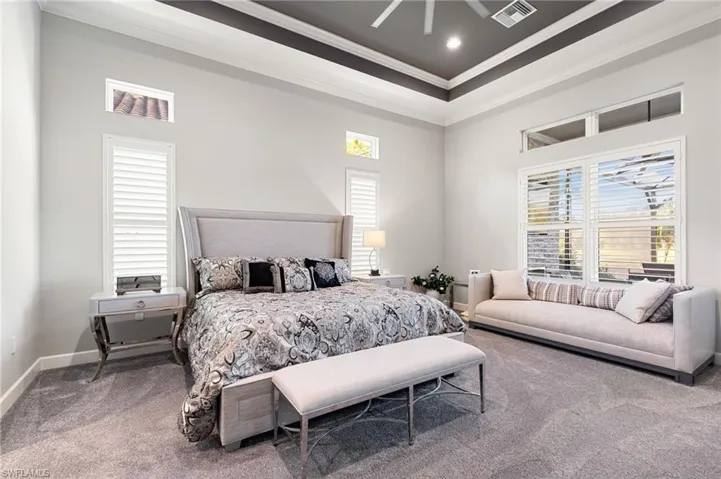 Carpeted bedroom with ornamental molding, ceiling fan, multiple windows, a towering ceiling, and a tray ceiling