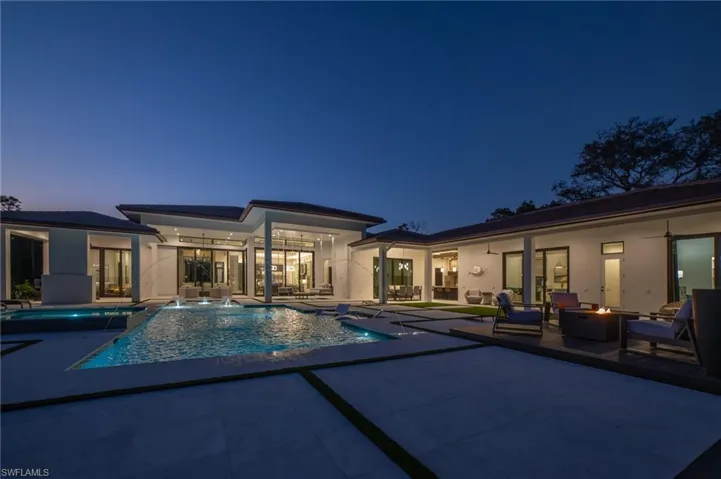 Pool at dusk with pool water features, ceiling fans, an outdoor fire pit, and plenty of outdoor space