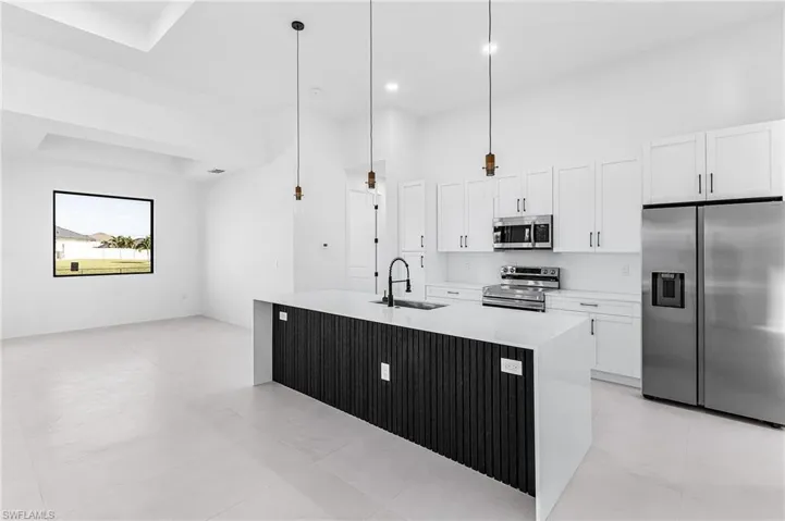Kitchen with appliances with stainless steel finishes, hanging light fixtures, white cabinetry, light stone countertops, and a towering ceiling