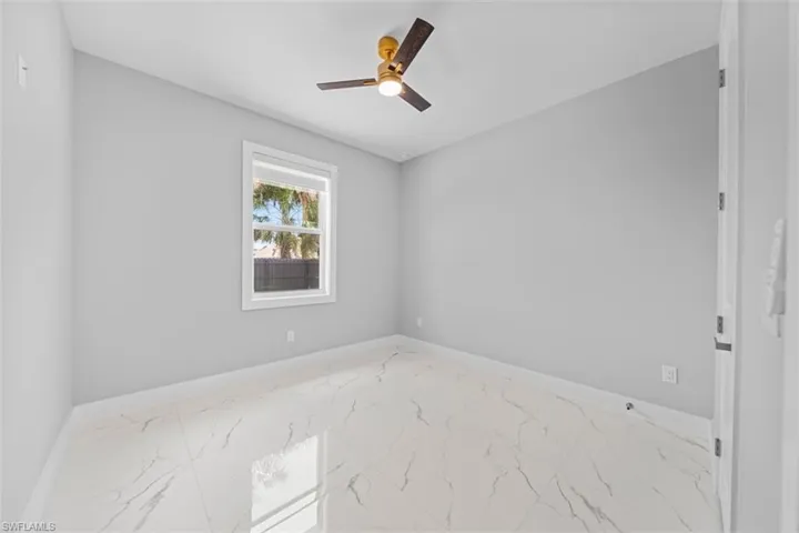 Bright interior space featuring white marble-look tile flooring, light gray walls, and a ceiling fan with integrated lighting