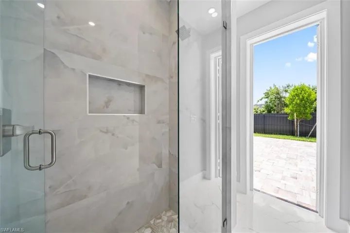 Glass-enclosed shower with large format marble-look tile walls, an integrated niche, and a hexagonal pebble tile floor