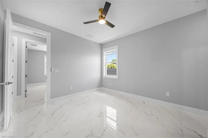 Spacious room featuring large format tile flooring, a modern ceiling fan with integrated lighting, a bright window, and a crisp white trim package