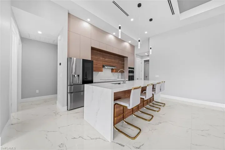 Modern kitchen featuring a large waterfall island with integrated seating, stainless steel appliances, marble-look flooring, and recessed lighting