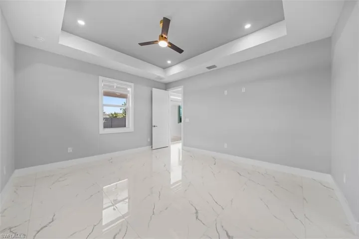 Spacious room featuring white porcelain tile flooring, a tray ceiling with recessed lighting, and a modern ceiling fan