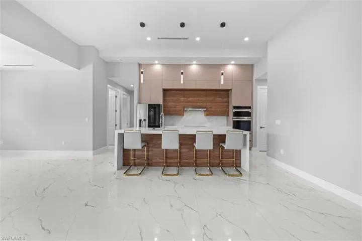 Open-concept living space featuring large format marble-look tile flooring, a kitchen island with seating for four, wood-finish cabinetry, integrated stainless steel appliances, and recessed lighting