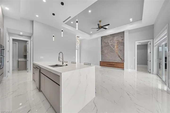 Open-concept living space with large format white tile flooring, a kitchen island featuring a waterfall countertop, recessed lighting, and a tray ceiling