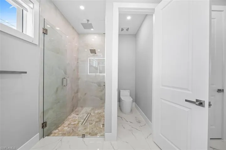 Contemporary bathroom featuring a spacious glass-enclosed shower with a rainfall showerhead and handheld sprayer, stone-finish wall tile, and pebble-style shower pan
