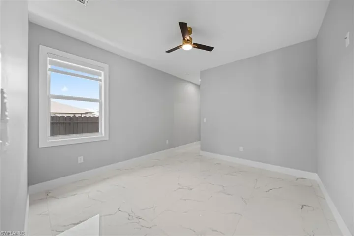 Spacious room featuring large format tile flooring, a modern ceiling fan with integrated lighting, a white framed window, and light grey painted walls
