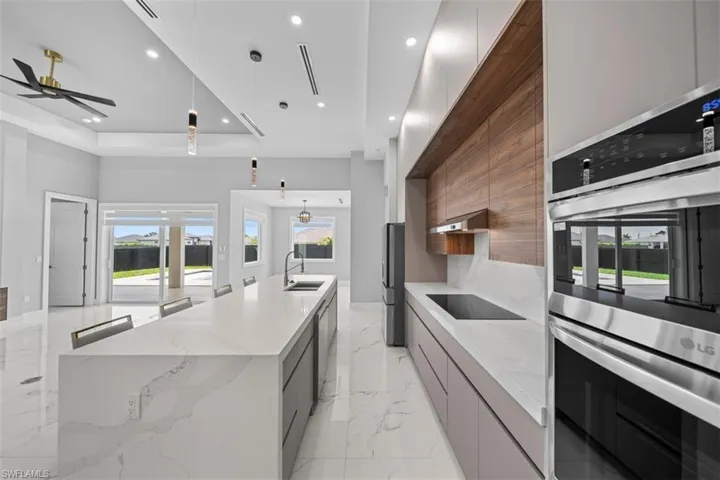 Contemporary kitchen featuring a large waterfall-edge island, integrated stainless steel appliances, wood-finish accent wall, and recessed lighting