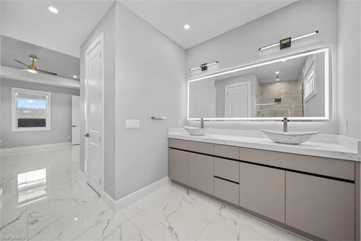 Dual vessel sinks set atop a contemporary vanity with a spacious countertop, illuminated by a large back-lit mirror and modern light fixtures