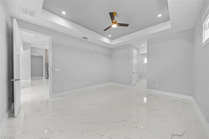 Spacious room featuring large format tile flooring, a tray ceiling with recessed lighting, and a modern ceiling fan