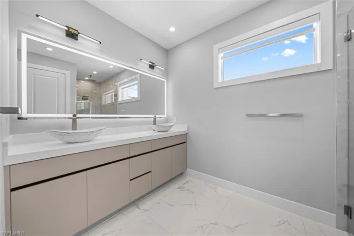 Dual vessel sinks atop a wide vanity with ample storage, featuring a large backlit mirror and integrated linear lighting