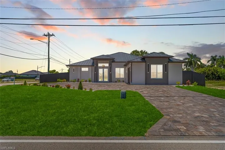 Contemporary stucco exterior with a dark tile roof, paver driveway, manicured lawn, and clear glass double entry doors