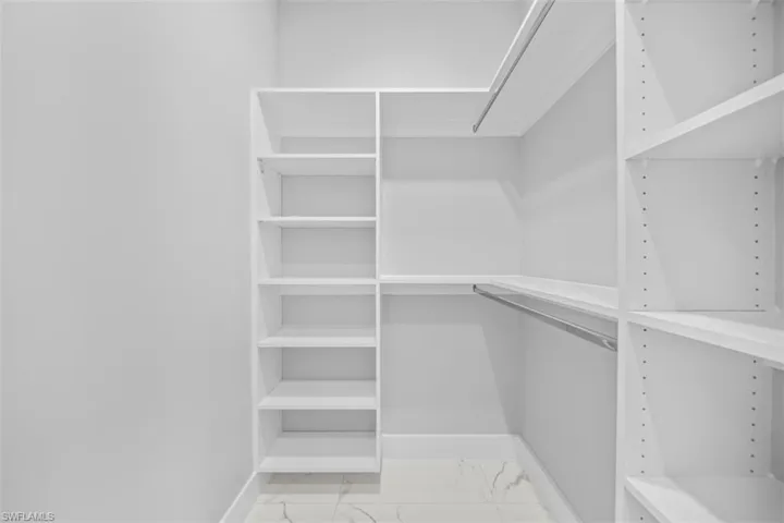 Built-in white shelving system with multiple storage racks and hanging rods, complemented by white baseboards and polished tile flooring