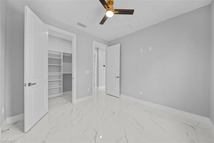 Spacious room featuring large format porcelain tile flooring, a ceiling fan with gold-tone accents, and a built-in closet with shelving