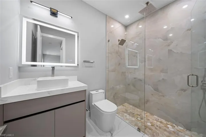 Modern bathroom featuring a glass-enclosed shower with large format stone-finish wall tile and pebble-finish floor