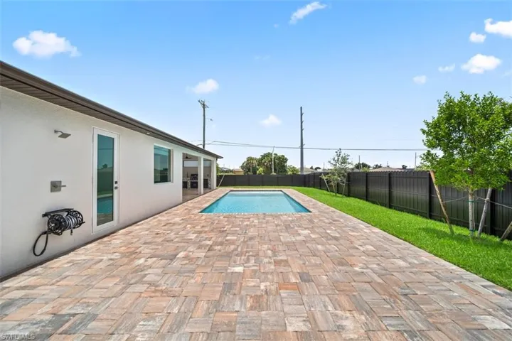 Expansive paver patio with an in-ground swimming pool, bordered by a manicured lawn and a dark privacy fence