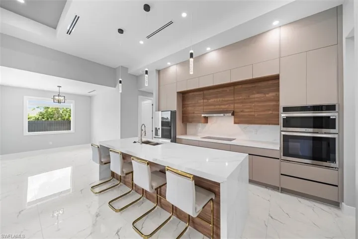 Modern kitchen featuring a large waterfall island with a white stone countertop, built-in stainless steel appliances, contemporary cabinetry, a wood-finish accent wall, and recessed lighting