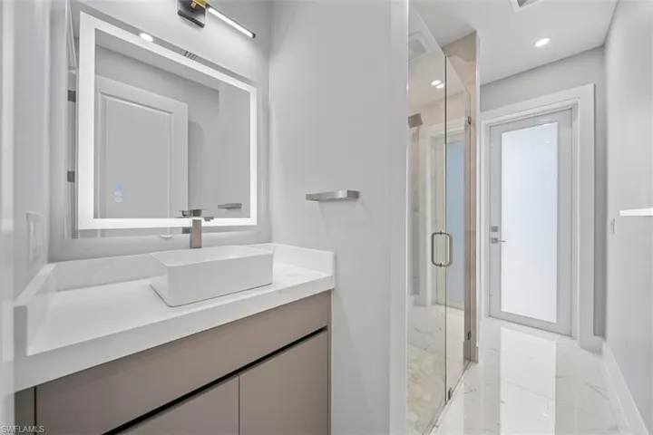 Contemporary bathroom featuring a vessel sink, quartz countertop, illuminated vanity mirror, and glass-enclosed shower