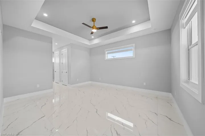 Spacious interior featuring large format tile flooring, a tray ceiling with recessed lighting and a ceiling fan, and multiple windows for natural light