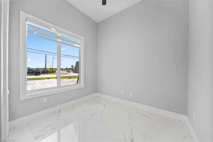 Interior space featuring large rectangular window, white trim, light gray walls, and white marble-look tile flooring