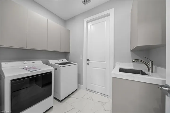 Laundry area featuring light gray cabinetry, a utility sink with a brushed nickel faucet, a white countertop, and large format marble-look tile flooring