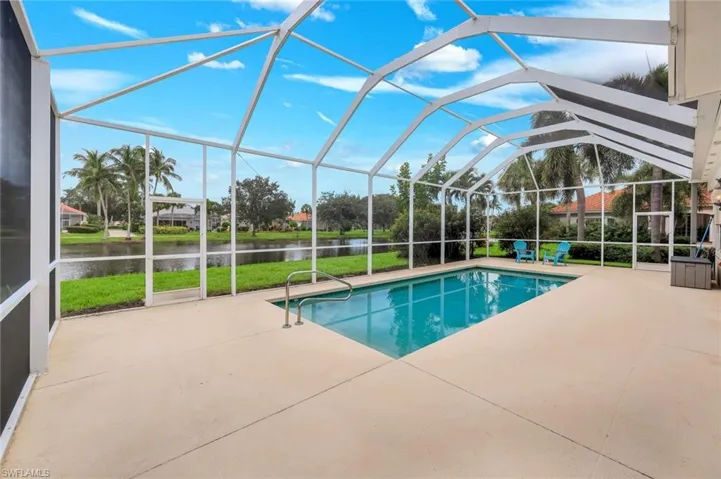 Screened enclosure with an in-ground swimming pool, concrete deck, and a water feature beyond