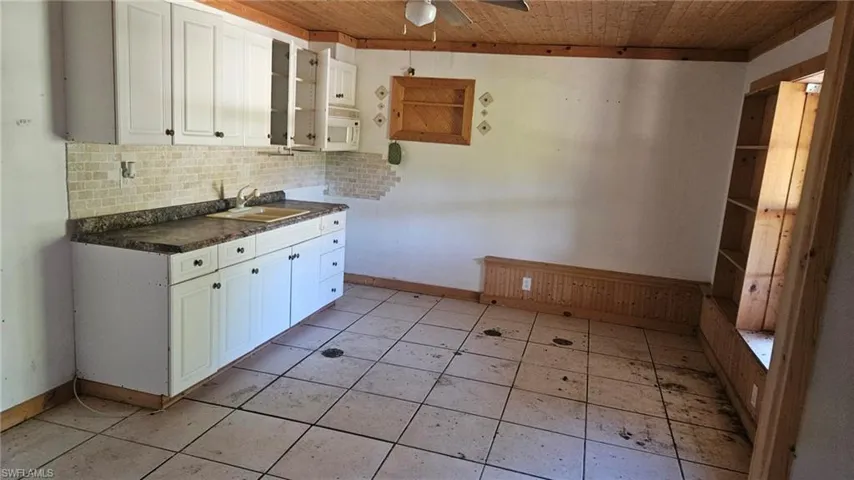 Kitchen with dark countertops, backsplash, white cabinetry, white microwave, and ceiling fan