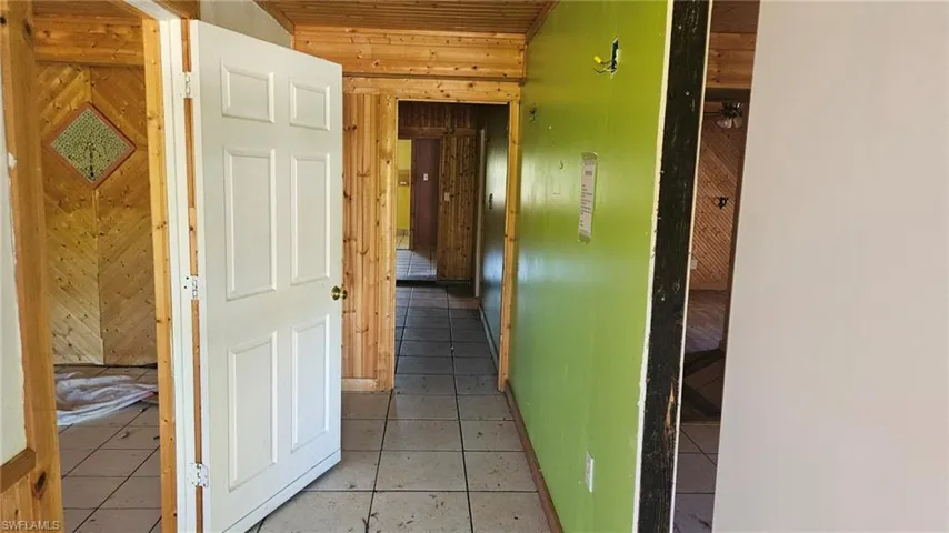 Hall with light tile patterned flooring, wooden walls, and wood ceiling