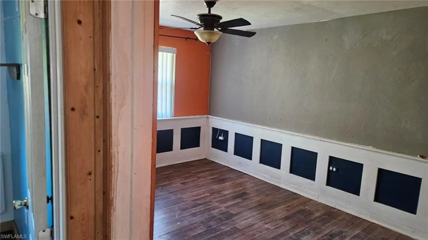 Spare room with dark wood-type flooring, a decorative wall, ceiling fan, and a wainscoted wall