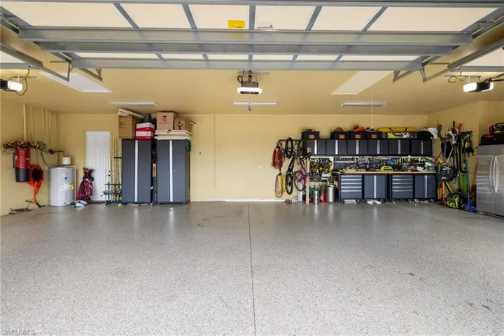 Garage with electric water heater, freestanding refrigerator, and a garage door opener
