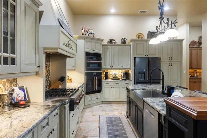 Two tone kitchen with two tone color scheme, light stone counters, tasteful backsplash, stainless steel appliances, and pendant lighting