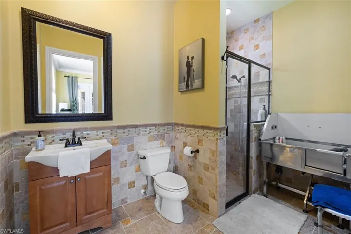 Full bath featuring vanity, a shower stall, wainscoting, and tile walls
