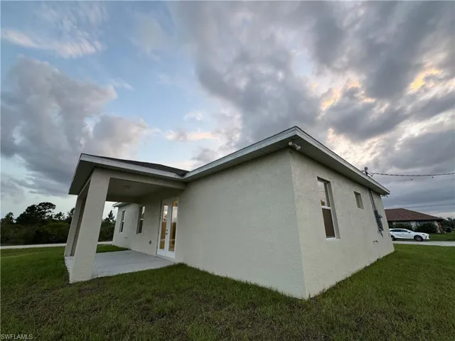 View of side of property featuring stucco siding, a lawn, and a patio area