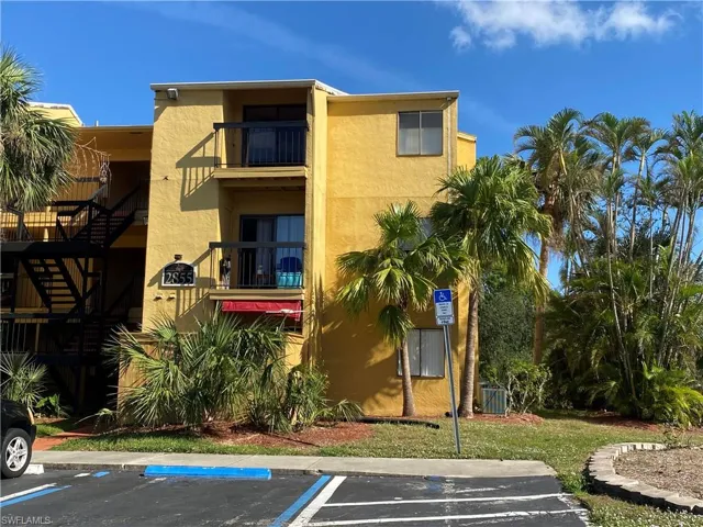 Multi-story exterior featuring a yellow stucco façade, dual stacked balconies with metal railings, and mature palm landscaping