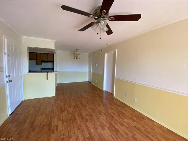 Living area featuring wood-finish flooring, two-tone wall treatment with chair rail molding, a multi-blade ceiling fan with integrated light fixture, and a pass-through opening to the kitchen