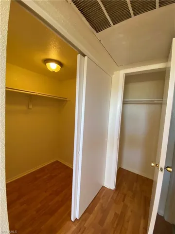 Storage area featuring wood-finish flooring, sliding panel doors, and built-in shelving with overhead lighting