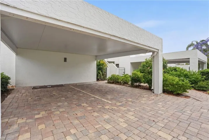 Covered parking area featuring a paver brick surface and stucco exterior