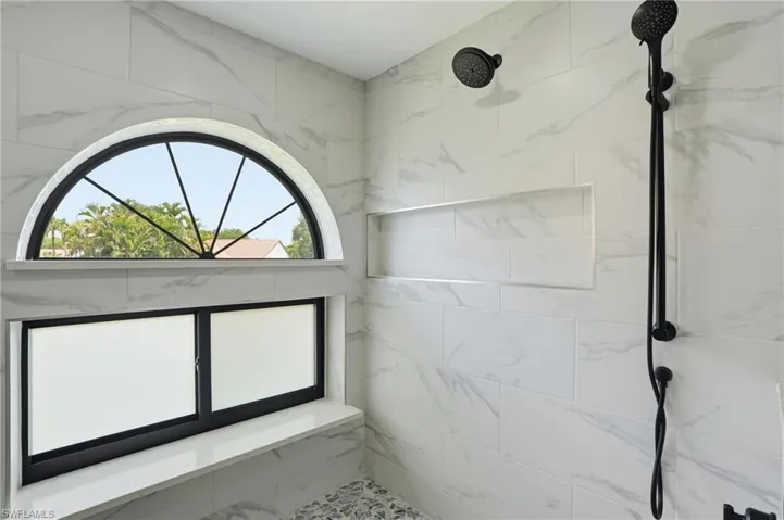 Shower enclosure featuring white marble-look subway tile, a rounded arch window with black mullions, and a frosted rectangular window